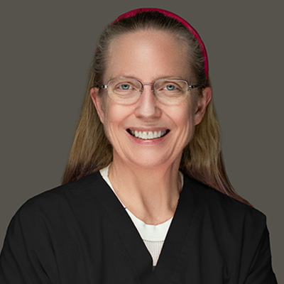 Portrait of a smiling female healthcare professional wearing glasses and a black scrub top, with a pink headband.
