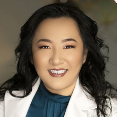 Portrait of a smiling woman in a white lab coat and teal blouse, looking at the camera.